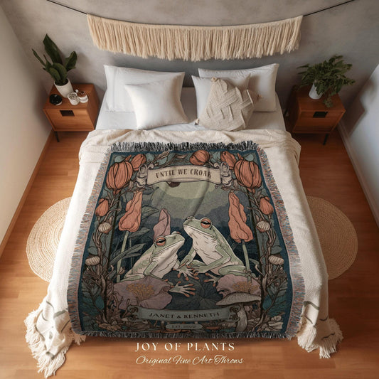 May include: A woven throw blanket featuring an illustration of two green frogs with the text "UNTIL WE CROAK". The blanket has a teal background with floral and mushroom accents. The bottom of the blanket reads "JOY OF PLANTS Original Fine Art Throws".