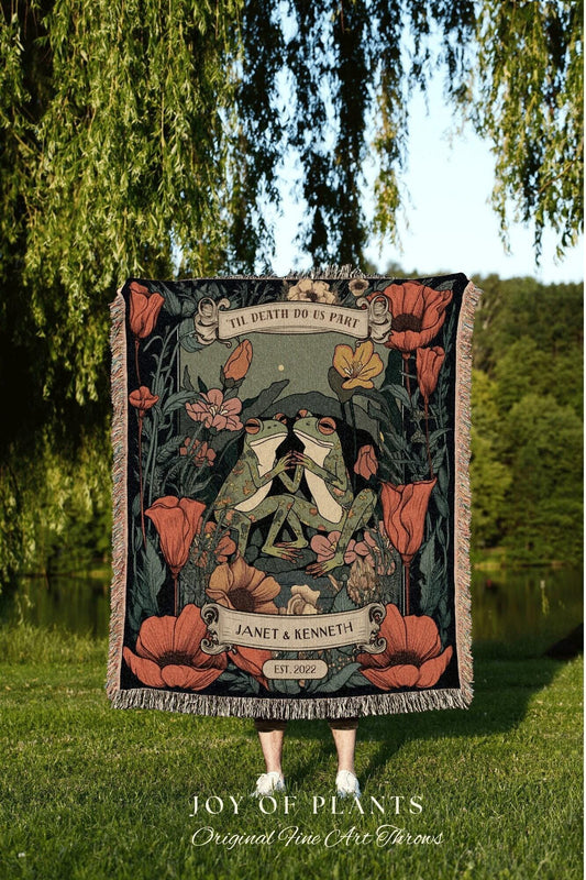 May include: A decorative throw blanket featuring a floral design with two embracing frogs. The blanket includes the text "TIL DEATH DO US PART" and the names "JANET & KENNETH" with the year "EST. 2022". The blanket has a fringed edge.