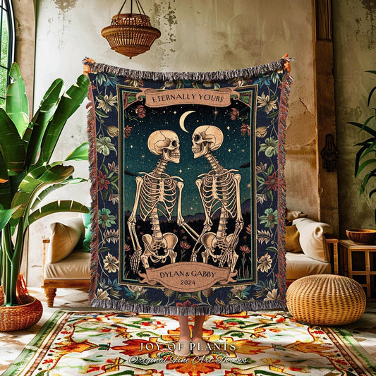 May include: A dark blue woven throw blanket featuring a romantic illustration of two skeletons holding hands under a starry night sky. The blanket has a decorative border with floral accents and the text "Eternally Yours" and "Dylan & Gabby 2024".