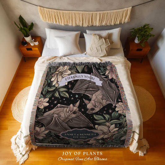 May include: A decorative throw blanket featuring a bat design with the text "Eternally Yours" and "Janet & Kenneth Est. 2022". The blanket has a black background with floral and leaf accents. The words "JOY OF PLANTS Original Fine Art Throws" are at the bottom.