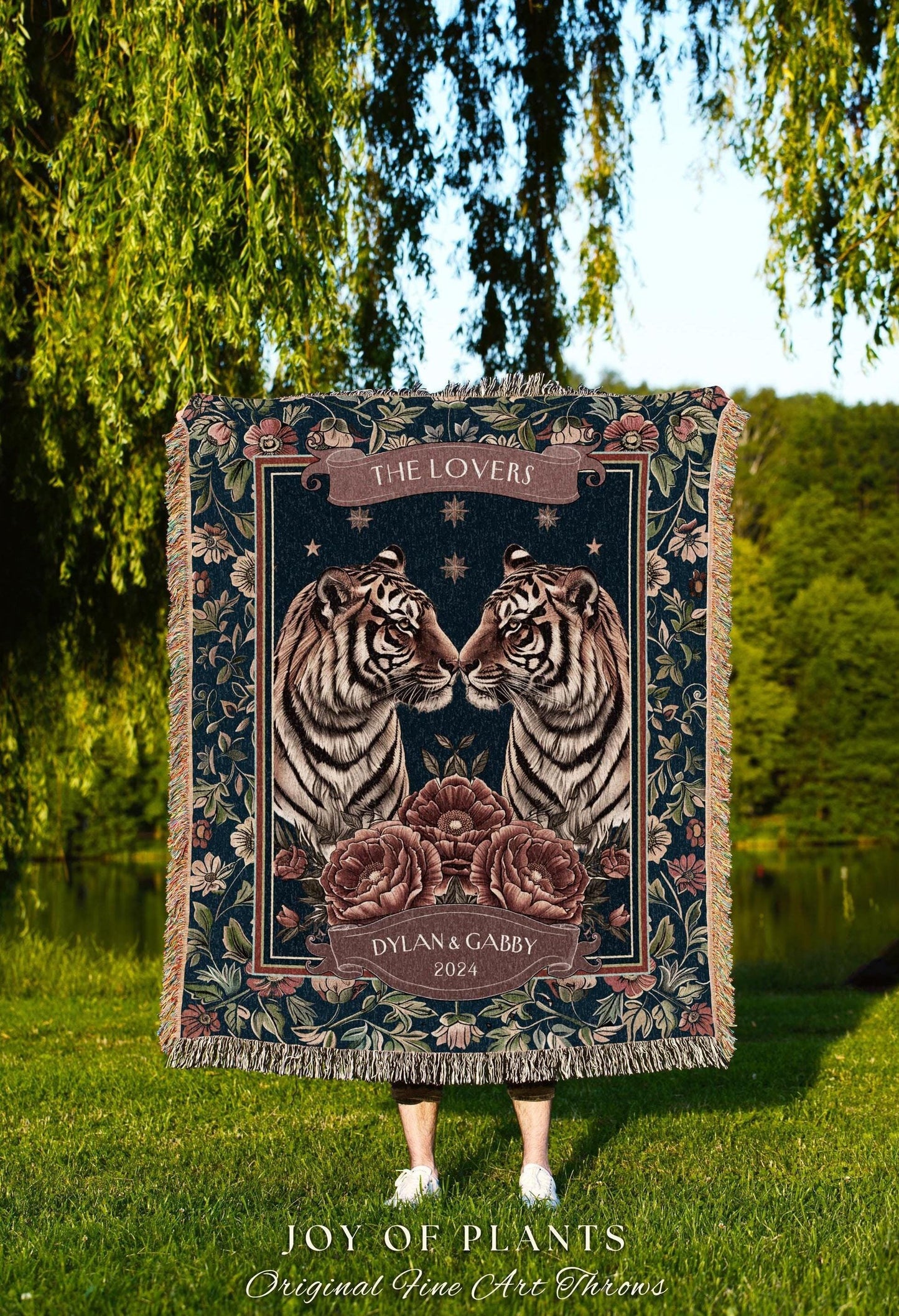 May include: A dark blue throw blanket featuring two facing tigers with floral and banner accents. The banner reads "THE LOVERS" and "DYLAN & GABBY 2024". The blanket has a fringed edge and is set against a natural background.