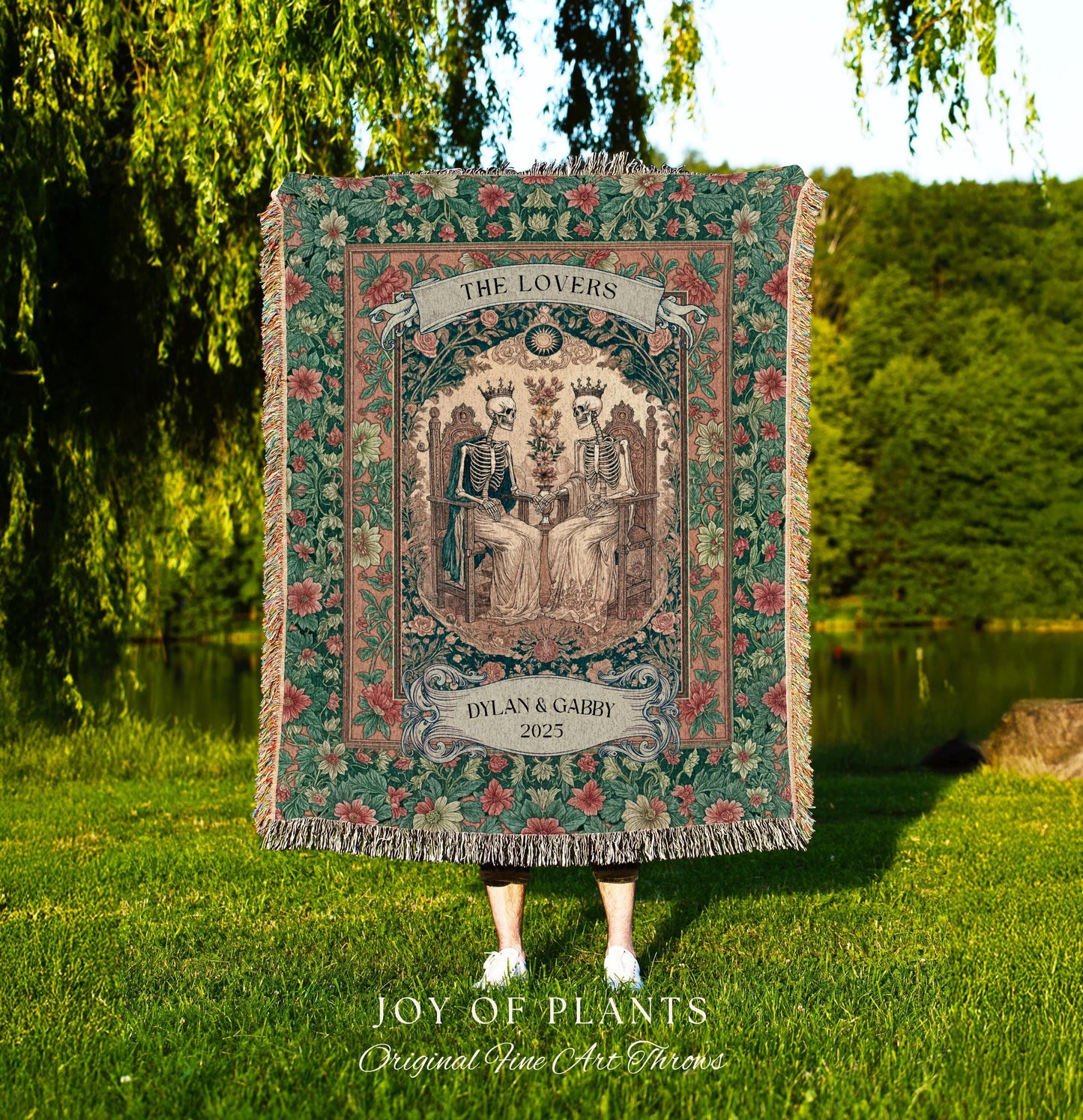 May include: A tapestry throw blanket with a floral border and a central image of two skeletons seated on thrones. The banner reads "THE LOVERS" above the image, and "DYLAN & GABBY 2025" below. The blanket is fringed.