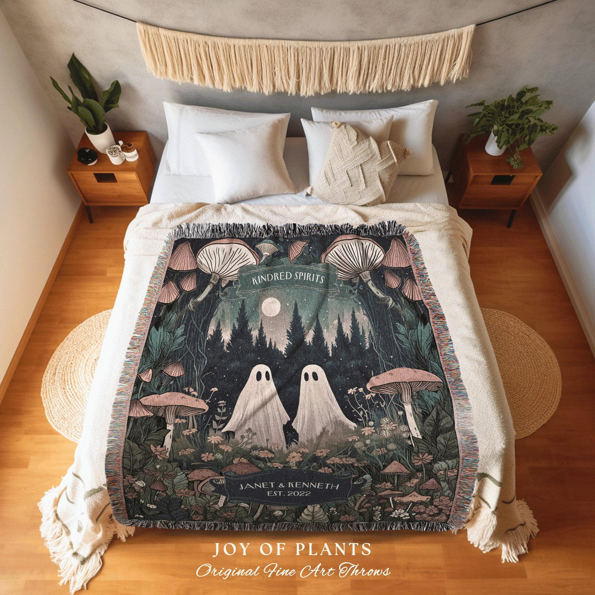 May include: A woven throw blanket featuring a forest scene with two ghost figures, mushrooms, and the text "KINDRED SPIRITS". The blanket has a cream-colored fringe and the text "JOY OF PLANTS" and "Original Fine Art Throws".