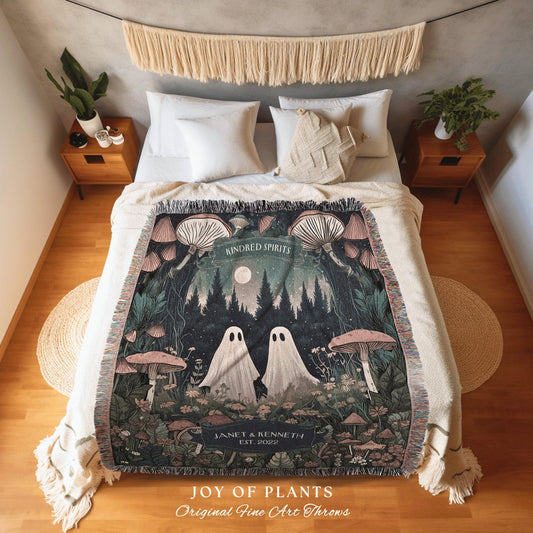 May include: A woven throw blanket featuring a forest scene with two ghost figures, mushrooms, and the text "KINDRED SPIRITS". The blanket has a cream-colored fringe and the text "JOY OF PLANTS" and "Original Fine Art Throws".