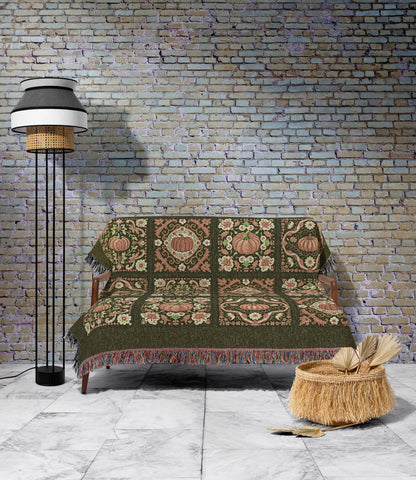 May include: A green throw blanket with a pumpkin and floral pattern draped over a wooden sofa. The blanket has a fringed edge and is decorated with pumpkins in shades of orange and pink. A woven basket with fringe sits on the floor.