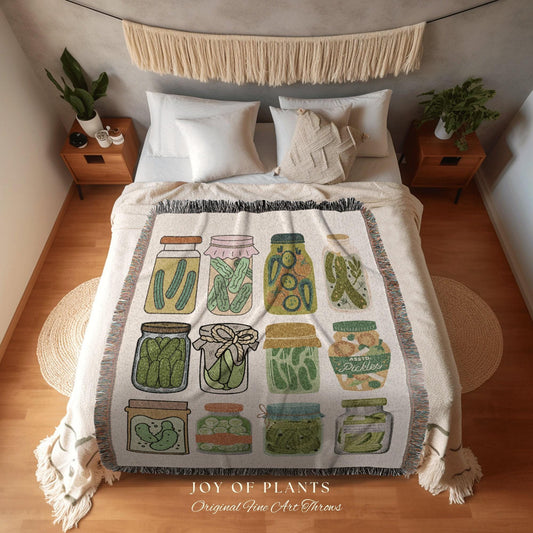 May include: A cream-colored throw blanket featuring illustrations of various pickle jars. The jars are filled with pickles and have different lid styles. The blanket has a fringed edge and the text "JOY OF PLANTS Original Fine Art Throws".