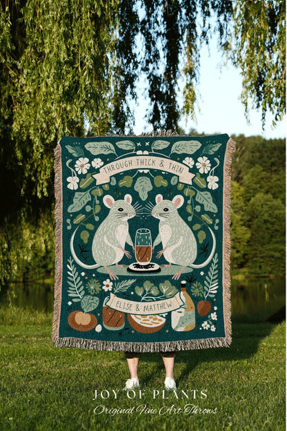 May include: A teal throw blanket with a whimsical design featuring two mice facing each other, a glass of liquid, and the text "THROUGH THICK & THIN." The blanket has a fringe border and the names "ELISE & MATTHEW" are displayed. The words "JOY OF PLANTS" and "Original Fine Art Throws" are also visible.